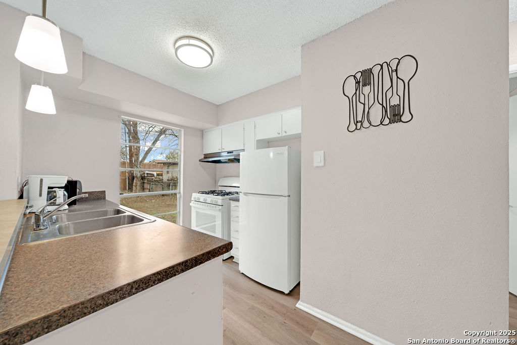 6706 Red Bluff Road San Antonio, TX 78218 - Photo 8 of 17 a kitchen with granite countertop a refrigerator a stove a sink and white cabinets with wooden floor