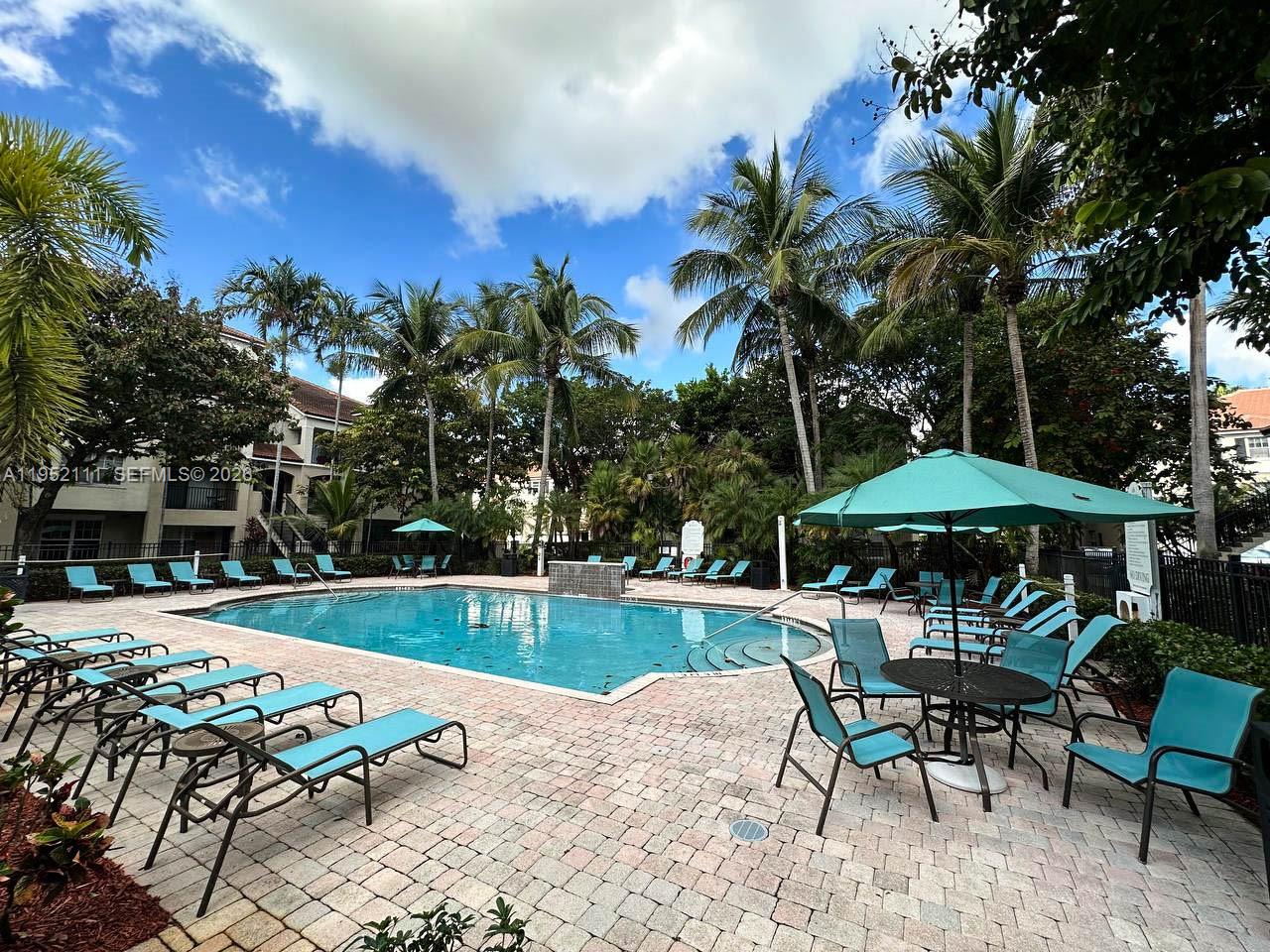 5840 West Sample Road, Unit 305 Coral Springs, FL 33067 - Photo 28 of 38 a view of a swimming pool with lawn chairs under an umbrella