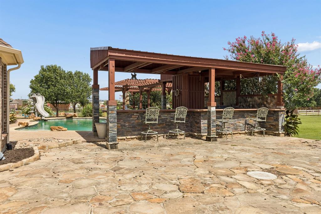 317 Singing Quail Trail Haslet, TX 76052 - Photo 27 of 32 Outdoor entertainment area featuring a stone patio, built-in bar with stacked stone accents, wooden pergola, and a swimming pool with a slide