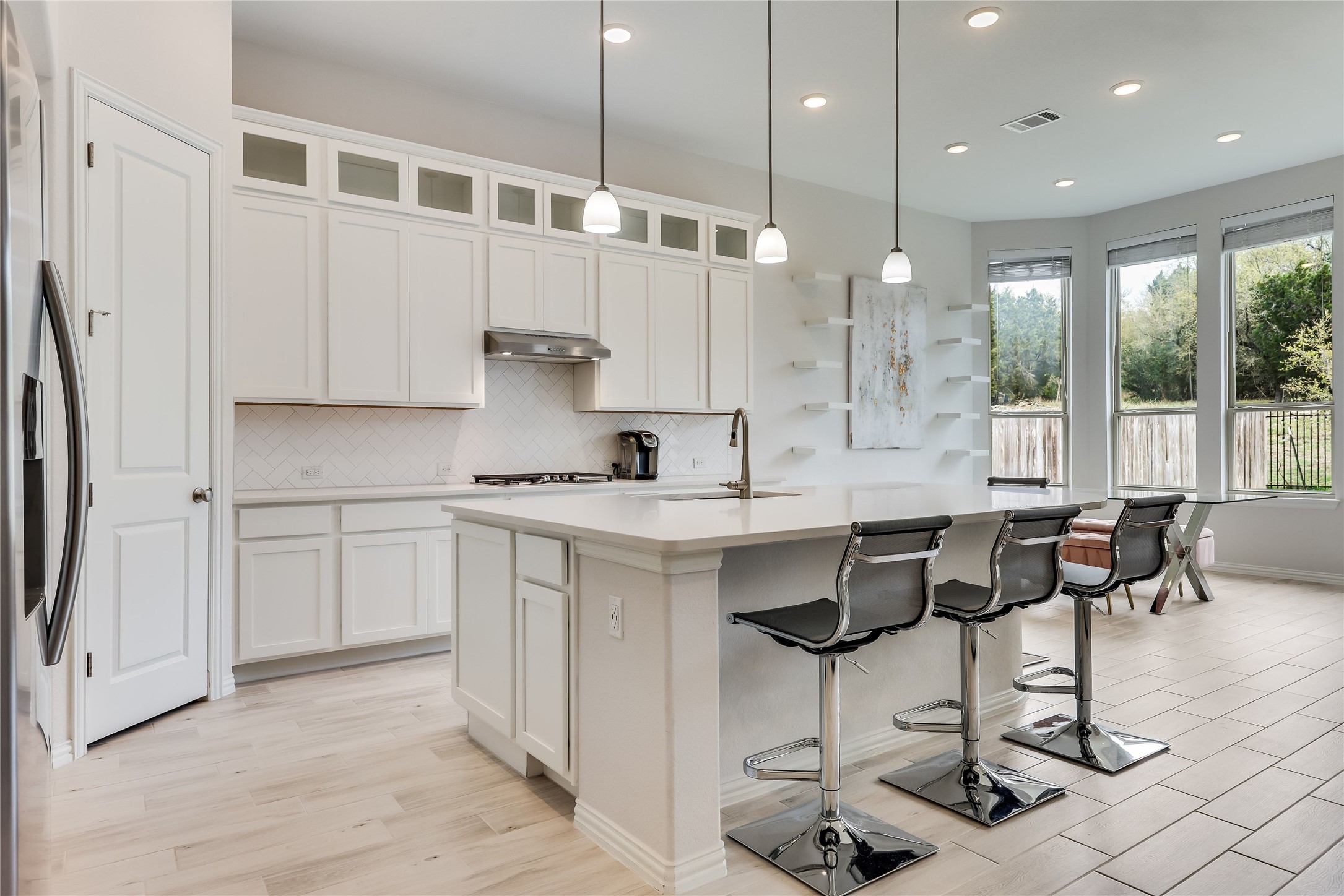 7705 Pace Ravine Drive Lago Vista, TX 78645 - Photo 10 of 40 Kitchen featuring decorative light fixtures, an island with sink, a kitchen breakfast bar, stainless steel fridge, and white cabinetry
