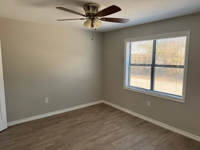an empty room with wooden floor fan and windows
