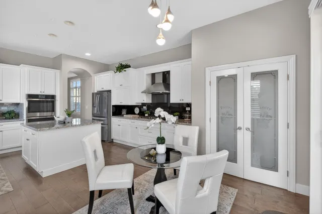 a kitchen with stainless steel appliances granite countertop a stove top oven a sink a refrigerator and chairs