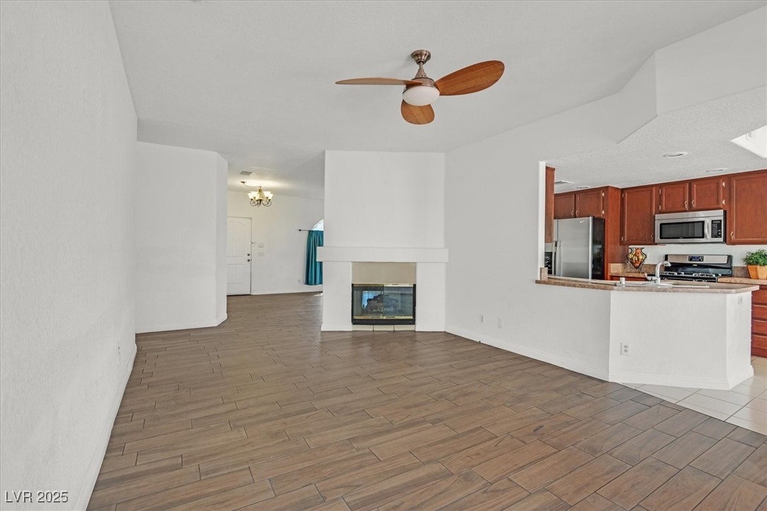 731 Rising Star Drive Henderson, NV 89014 - Photo 5 of 25 Unfurnished living room with a ceiling fan, light wood finished floors, a chandelier, and a multi sided fireplace