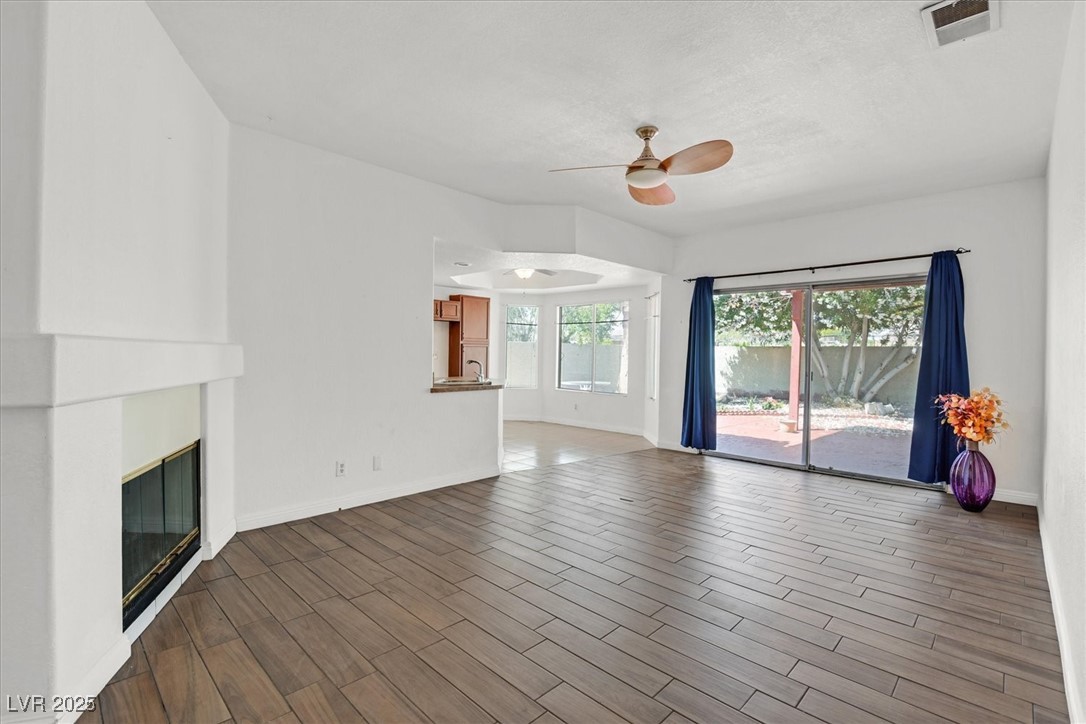 731 Rising Star Drive Henderson, NV 89014 - Photo 6 of 25 Unfurnished living room featuring a ceiling fan, a glass covered fireplace, baseboards, and wood finished floors