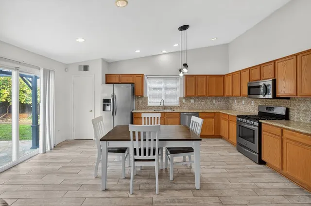 a kitchen with stainless steel appliances granite countertop a stove top oven a refrigerator a sink and a dining table with wooden floor