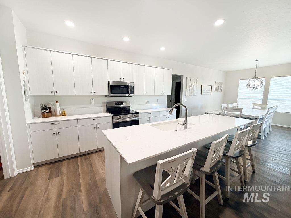 13694 Oliver Street Caldwell, ID 83607 - Photo 8 of 28 Kitchen with a kitchen bar, stainless steel appliances, white cabinetry, a kitchen island with sink, and dark wood-style flooring