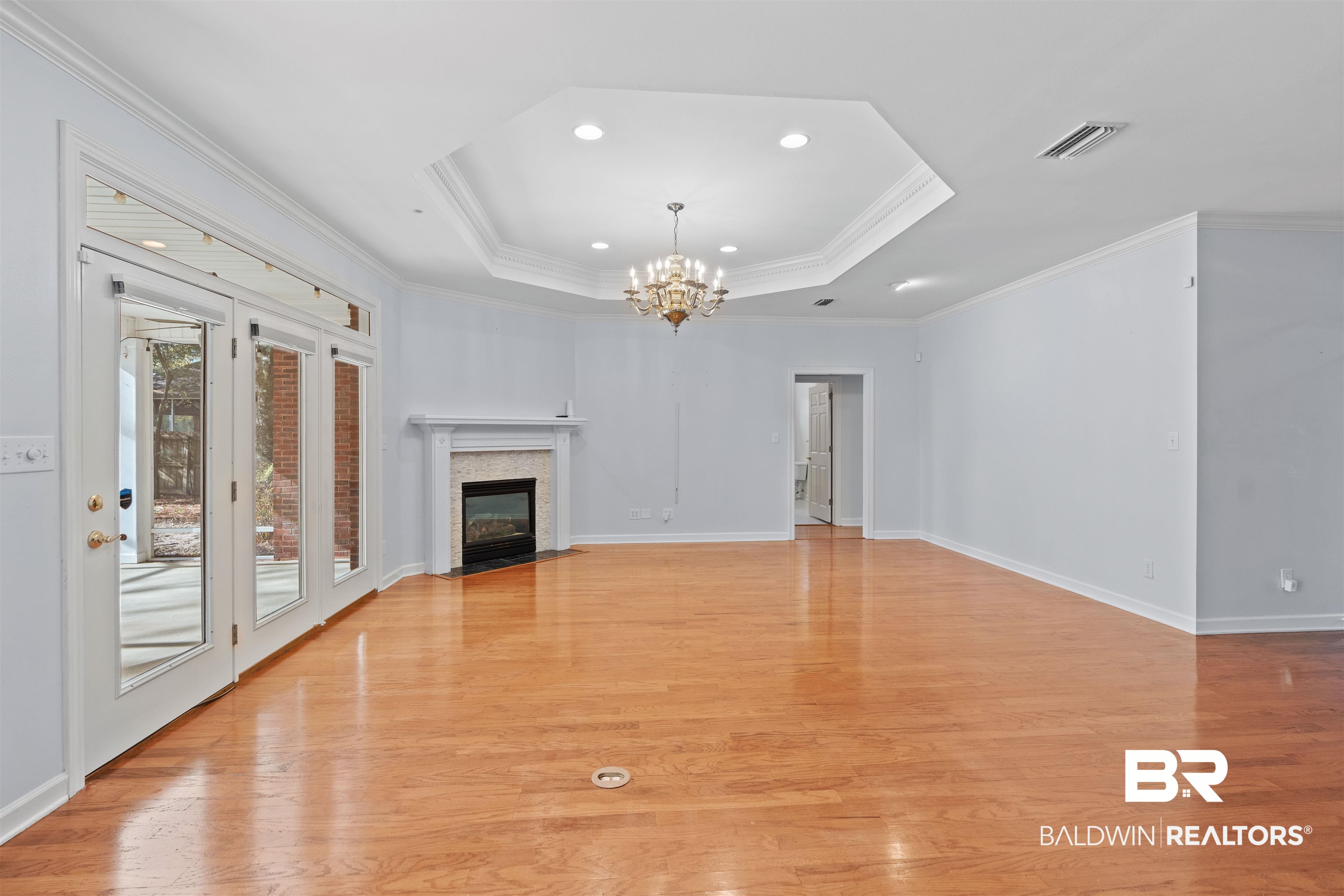 4 Judd Trail Daphne, AL 36527 - Photo 7 of 45 Unfurnished living room featuring visible vents, a notable chandelier, ornamental molding, a tray ceiling, and light wood-style floors