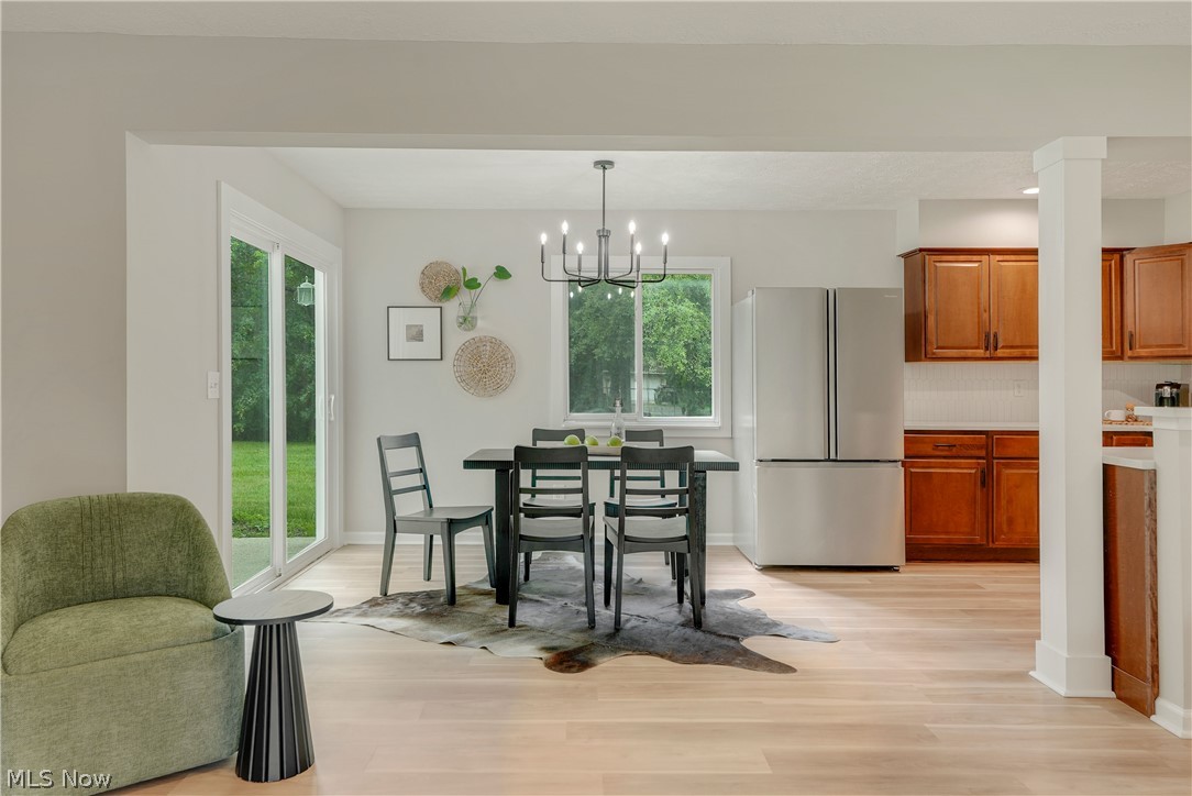 646 Ledge Road Macedonia, OH 44056 - Photo 5 of 28 Open concept dining area featuring light wood-finish flooring, a sliding glass door to the exterior, a modern chandelier, a window with exterior views, and an opening to the kitchen with wood cabinetry and stainless steel appliances