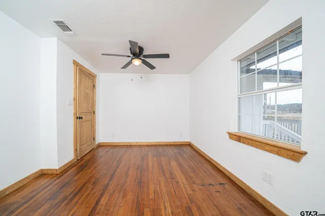 a view of empty room with wooden floor and fan