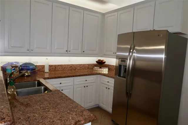 a kitchen with stainless steel appliances granite countertop a refrigerator a sink and white cabinets