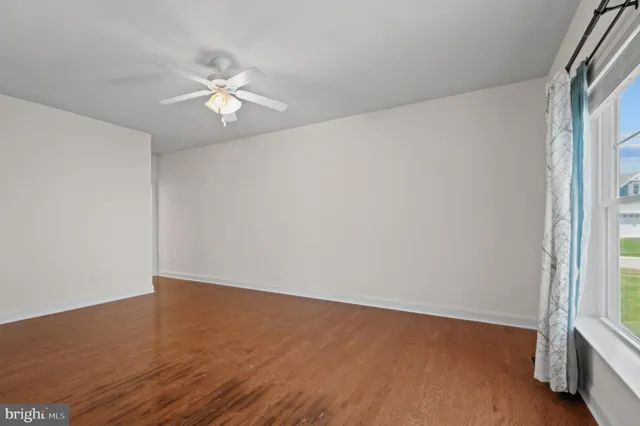 an empty room with wooden floor fan and windows