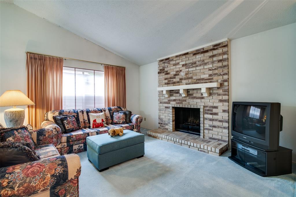 1916 Cobblestone Lane Garland, TX 75042 - Photo 11 of 33 Carpeted living area with vaulted ceiling, a brick fireplace, and a textured ceiling