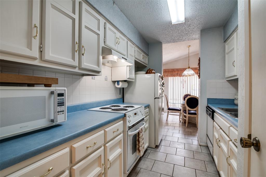 1916 Cobblestone Lane Garland, TX 75042 - Photo 16 of 33 Kitchen with white appliances, a textured ceiling, lofted ceiling, under cabinet range hood, and backsplash