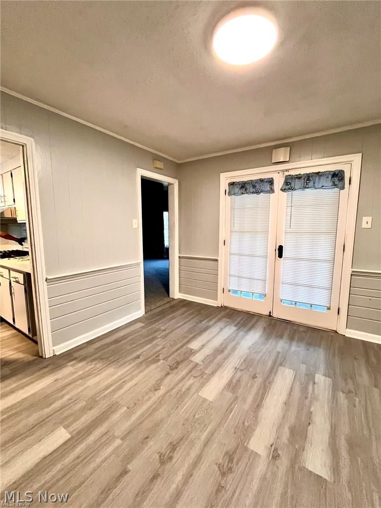 2752 Copley Road Akron, OH 44321 - Photo 14 of 35 Empty room with french doors, light wood-type flooring, a textured ceiling, ornamental molding, and a wainscoted wall