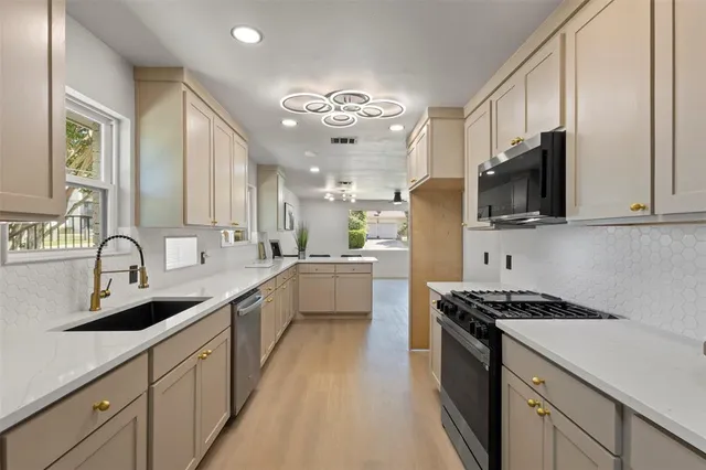 a kitchen with stainless steel appliances a sink dishwasher a stove top oven a refrigerator with white cabinets and wooden floor