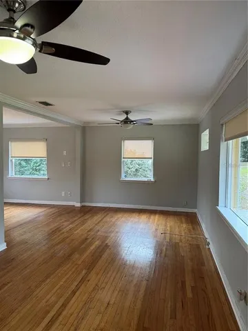 an empty room with wooden floor fan and windows