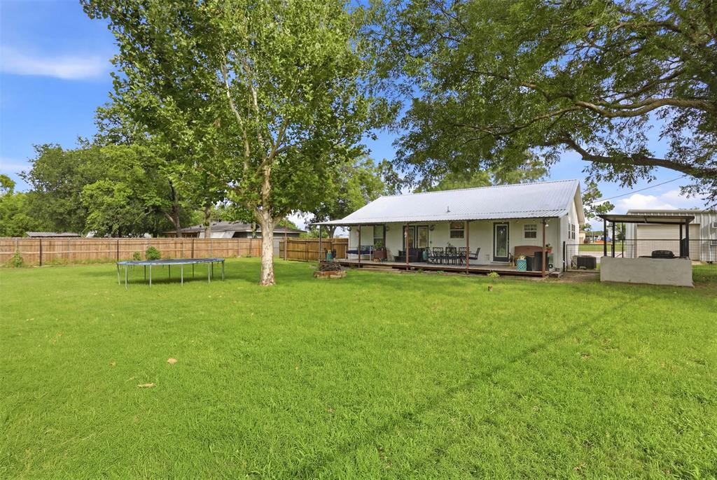 308 West 1st Street Springtown, TX 76082 - Photo 29 of 39 Expansive green lawn with mature trees and a wood fence border