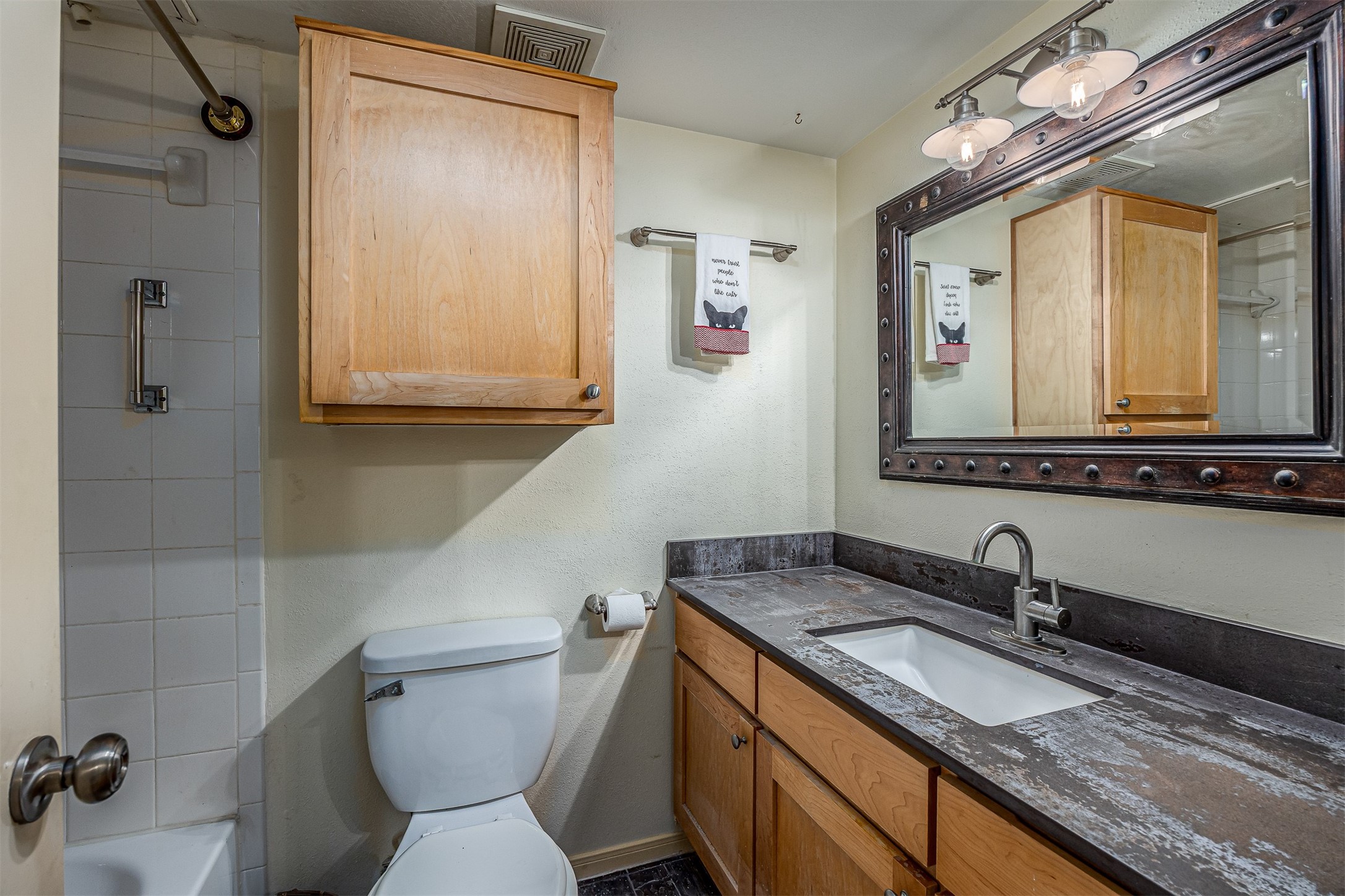 1505 Ward Road, Unit 128 Baytown, TX 77520 - Photo 17 of 21 This secondary bathroom features a shower-tub combo, a toilet, and a vanity with a dark stone countertop. It includes a large mirror with rustic framing and wooden cabinets for storage.