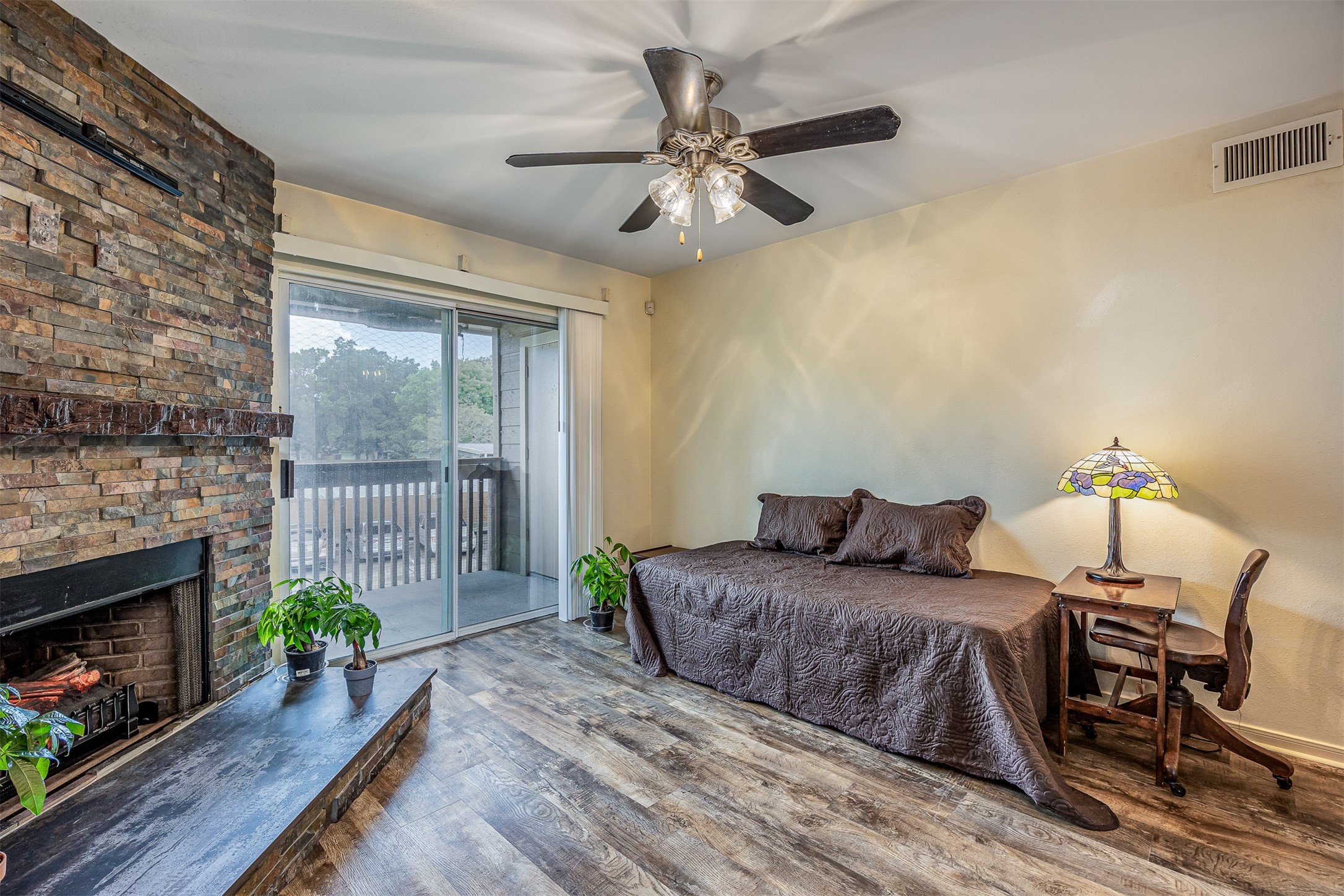 1505 Ward Road, Unit 128 Baytown, TX 77520 - Photo 4 of 21 This cozy room features a stone fireplace, wood look flooring, and a ceiling fan. It opens to a balcony through sliding glass doors, providing natural light and a view.