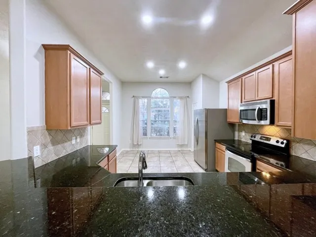 a view of a kitchen with kitchen island granite countertop a sink refrigerator stove and microwave