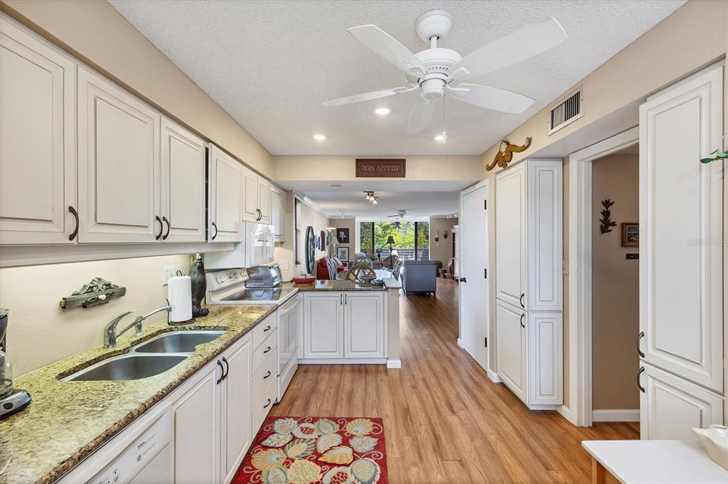 825 Bayport Way, Unit 825 Longboat Key, FL 34228 - Photo 32 of 62 a kitchen with granite countertop a refrigerator a sink dishwasher stove and white cabinets with wooden floor