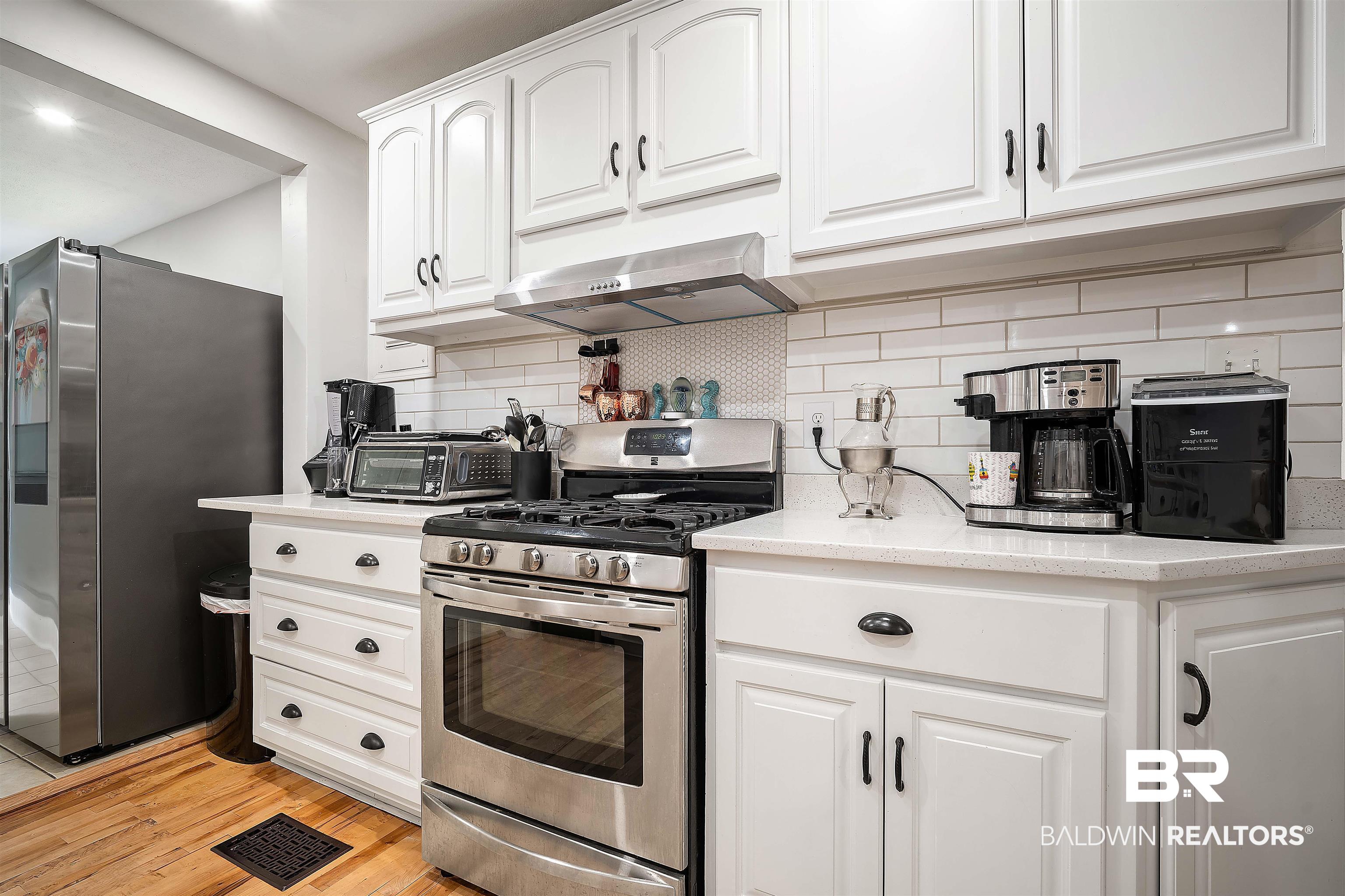 103 Emogene Place Mobile, AL 36606 - Photo 12 of 32 Kitchen featuring stainless steel appliances, white cabinetry, backsplash, light wood-style flooring, and light stone counters