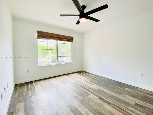 an empty room with wooden floor fan and windows