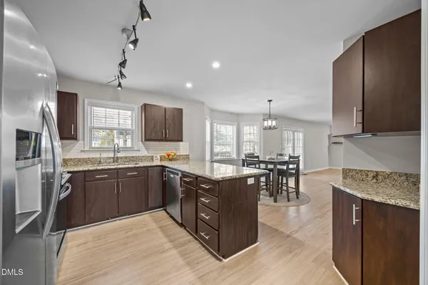 a kitchen with stainless steel appliances granite countertop a stove top oven a sink dishwasher a dining table and chairs with wooden floor