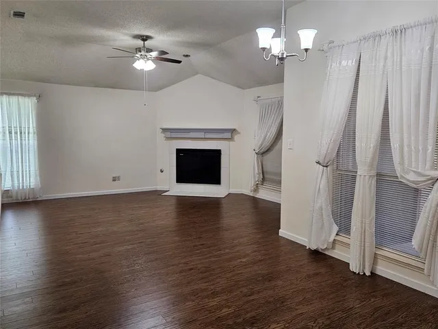 an empty room with wooden floor chandelier fan and windows