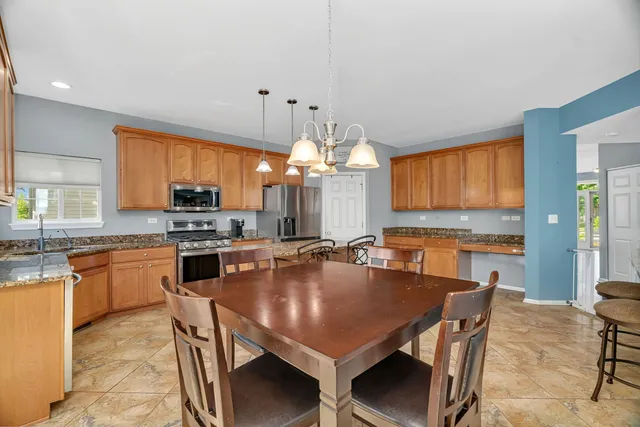 a kitchen with stainless steel appliances granite countertop a stove a refrigerator a kitchen island a dining table and chairs