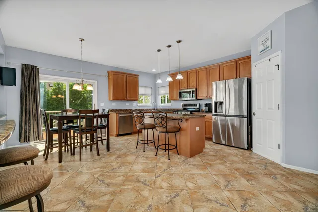 a kitchen with stainless steel appliances granite countertop a stove a refrigerator a kitchen island a stove a dining table and chairs with wooden floor