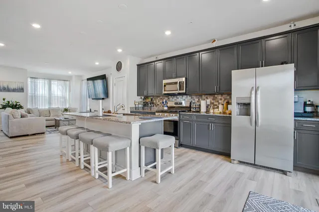 a kitchen with stainless steel appliances granite countertop a refrigerator a stove top oven a sink dishwasher and white cabinets with wooden floor