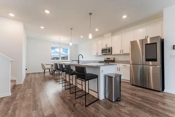 a kitchen with stainless steel appliances granite countertop a refrigerator a stove top oven a sink dishwasher a dining table and chairs with wooden floor