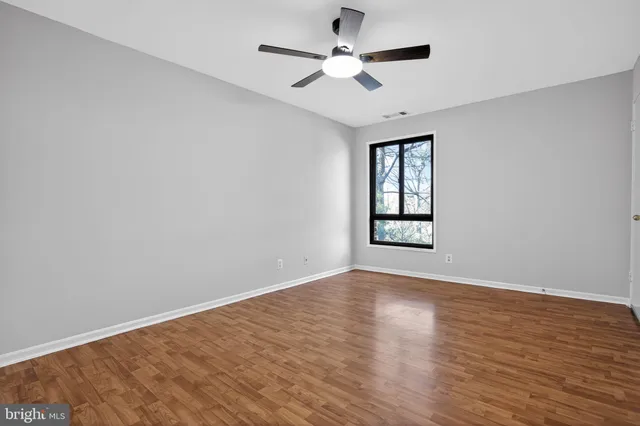 an empty room with wooden floor ceiling fan and windows