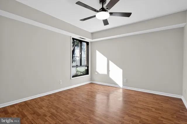an empty room with wooden floor fan and windows