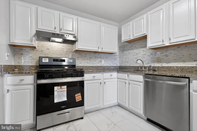 a kitchen with granite countertop white cabinets and stainless steel appliances