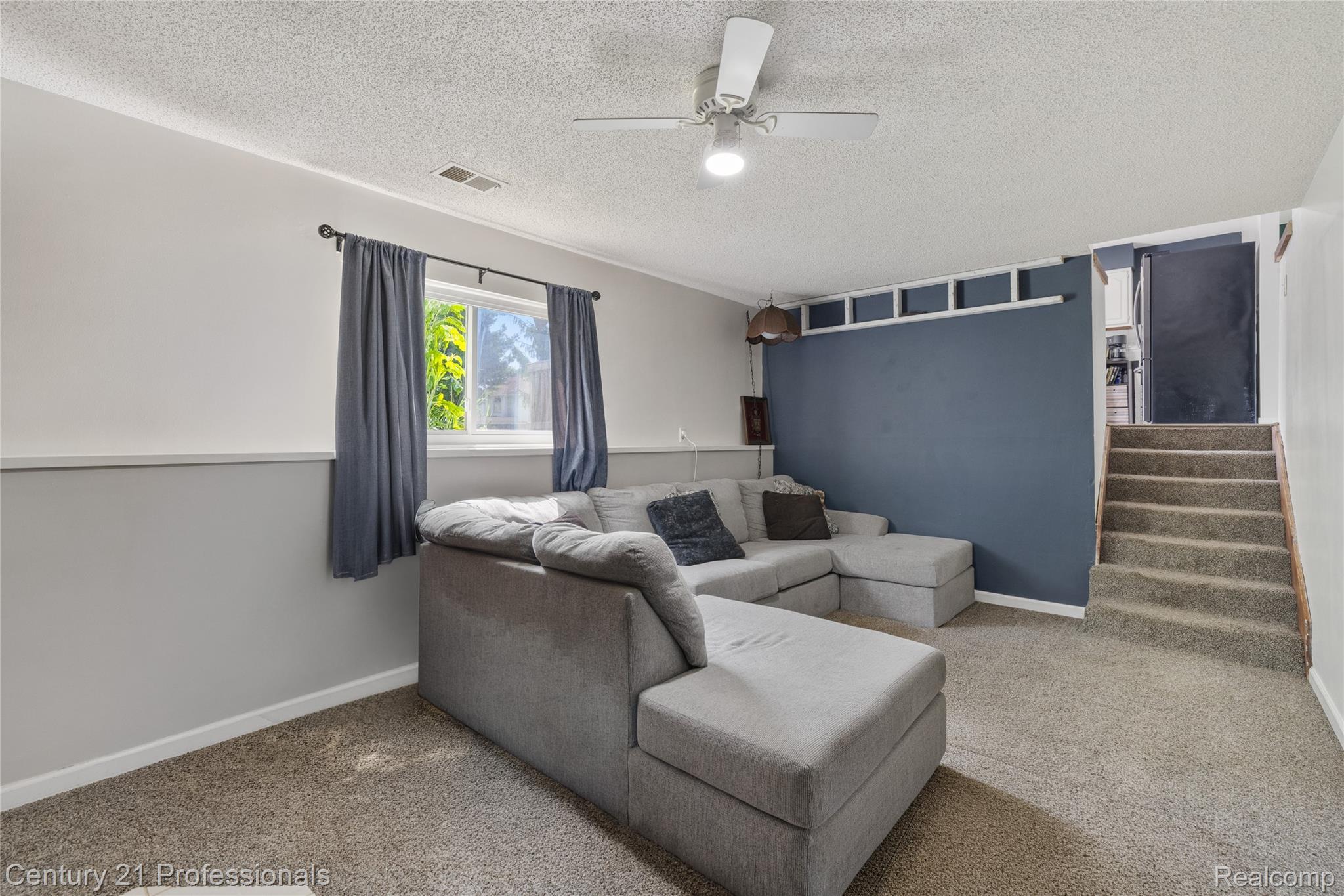 15037 Hogan Road Linden, MI 48451 - Photo 14 of 38 Carpeted room featuring a window with natural light, a ceiling fan with integrated lighting, a two-tone painted wall, and a staircase with carpeted treads
