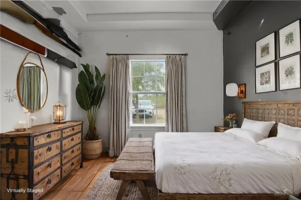 a bedroom with a bed a mirror on the dresser and a large window