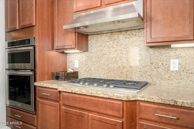 a kitchen with stainless steel appliances granite countertop a stove top oven a refrigerator a sink and chairs