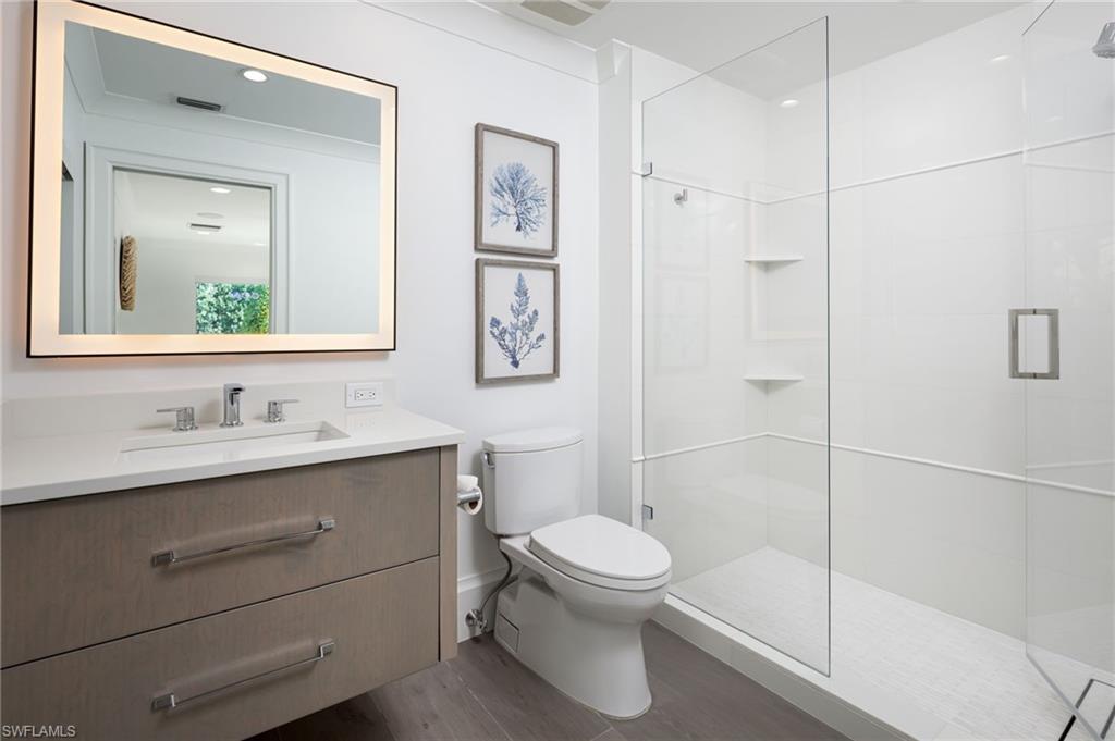 512 Neapolitan Lane Naples, FL 34103 - Photo 21 of 35 a bathroom with a toilet a sink a glass door a shower and a mirror