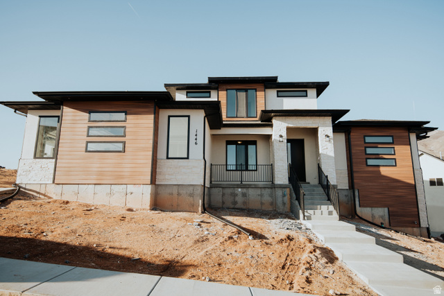 Contemporary exterior featuring multi-level architecture, wood-finish siding, stone accents, black-framed windows, and a concrete pathway leading to the main entrance