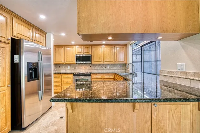 a kitchen with granite countertop stainless steel appliances a refrigerator counter space cabinetry and a large window