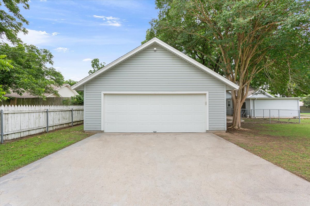 1607 North Harding Avenue Cameron, TX 76520 - Photo 34 of 37 A detached garage with gray siding and a white door offers ample parking and storage, complemented by a concrete driveway.