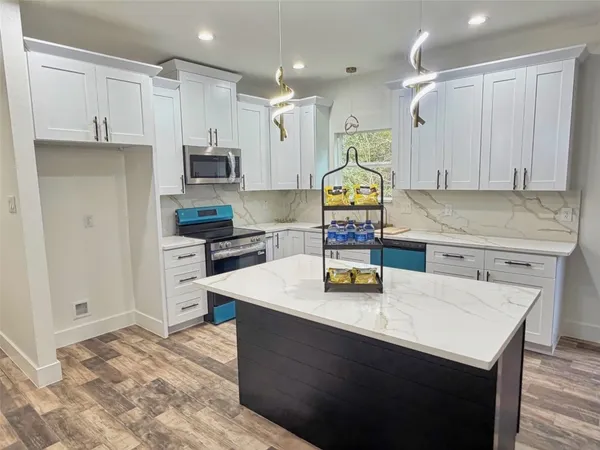 a kitchen with stainless steel appliances kitchen island granite countertop a sink dishwasher a stove and a refrigerator with wooden floor