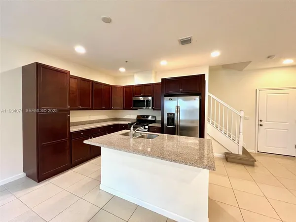 a large kitchen with stainless steel appliances kitchen island granite countertop a refrigerator and a sink