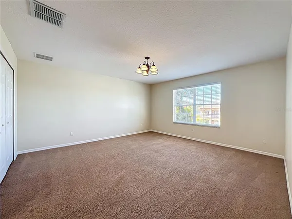 an empty room with a chandelier fan and wooden floor