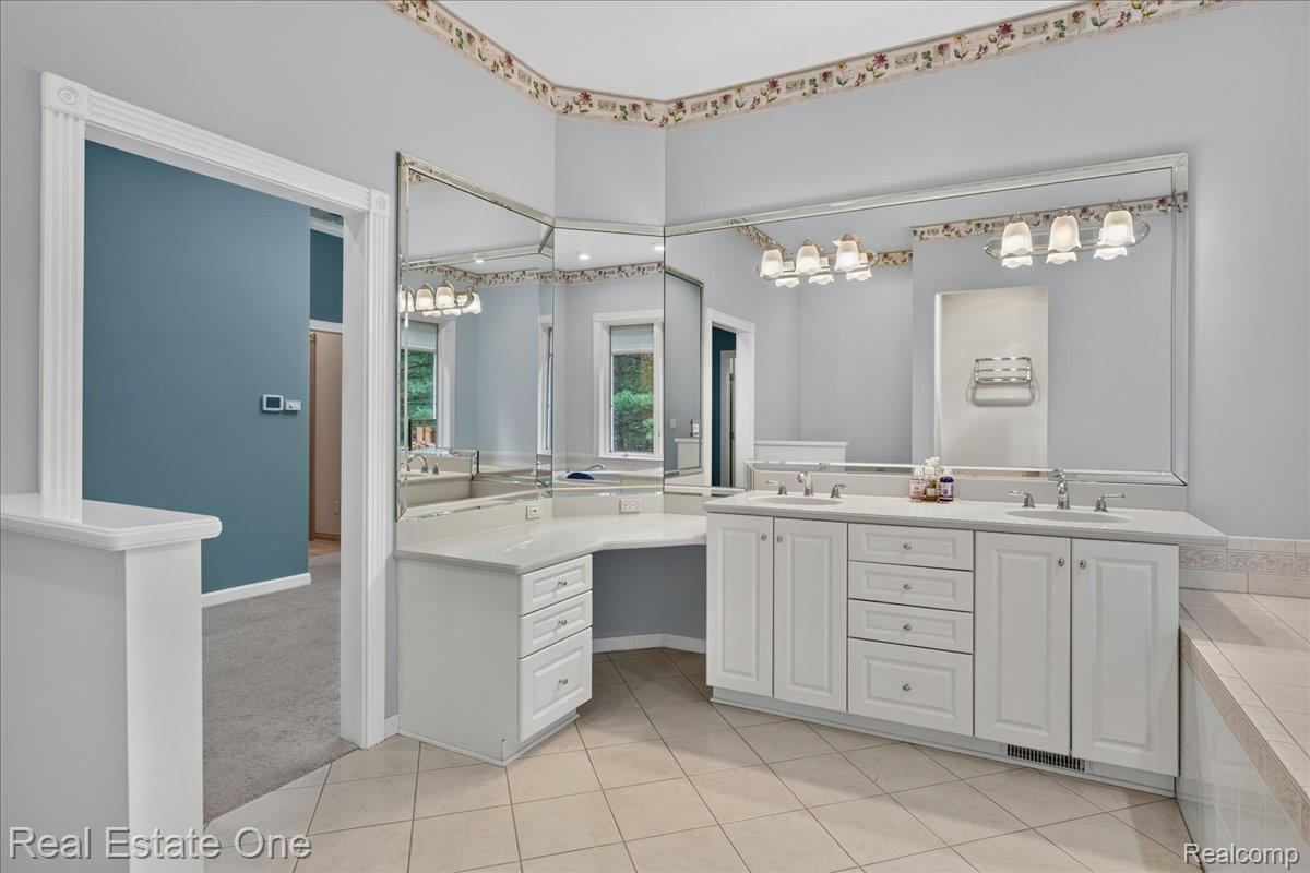 425 Courtney Road Leonard, MI 48367 - Photo 45 of 89 Vanity area featuring dual sinks, white cabinetry, integrated dressing table, and a large wall-mounted mirror