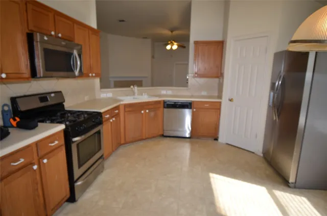 a large kitchen with stainless steel appliances granite countertop a refrigerator a sink dishwasher a stove and a dining table with wooden floor