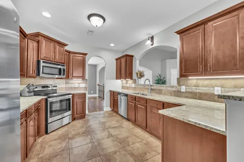 a large kitchen with stainless steel appliances granite countertop a stove top oven a sink dishwasher and wooden cabinets