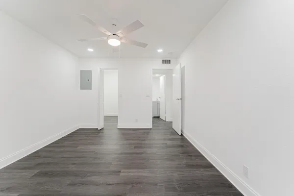 a view of an empty room with wooden floor and a ceiling fan
